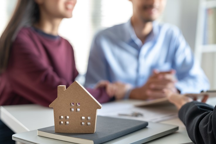 A cutout of a home in the front. A blurred man and a woman talking to someone in the background.